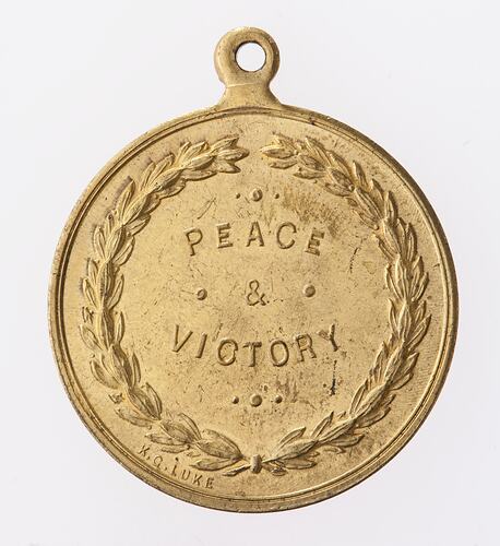 Round gold coloured medal with text surrounded by wreath.