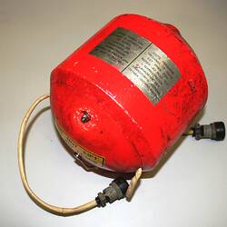 Bright orange-red metal cylindrical casing with domed ends, plates and labels. Two cords fixed at ends.