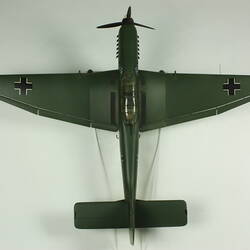 Model aeroplane. Dark green with a black cross on each wing tip. Propeller at front. Top view.