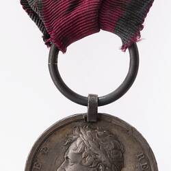Tarnished silver medal with bust of man facing left. Suspended from ring and red ribbon.