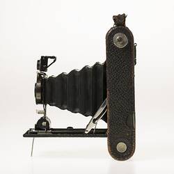 Black camera with leather covering. Folds out with bellows, metal brackets. Left profile.