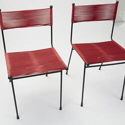 Two metal chairs strung with red cord seats and back sections. Top right view.