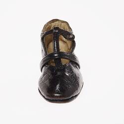 Miniature hand-sewn black leather shoe with strap and glass button fastener. Front view.
