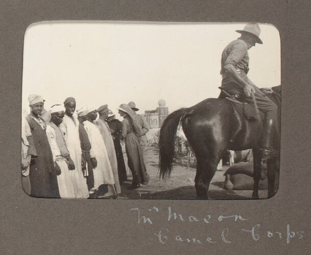 Uniformed man on horse with men in tunics watching.