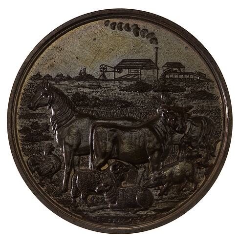 Round medal with pastoral scene in front and two building in distance.