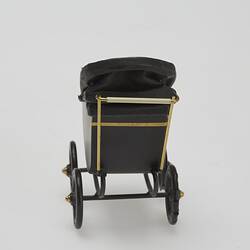 Painted black metal miniature pram with gold painted highlights and folding leather hood. Back view.