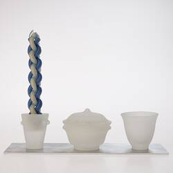 Opaque glass set on metal tray. Candle holder with woven blue white candle, lidded spice container and cup.