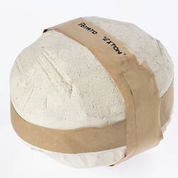 Round plaster mould with brown tape around top and side. Black writing on tape.