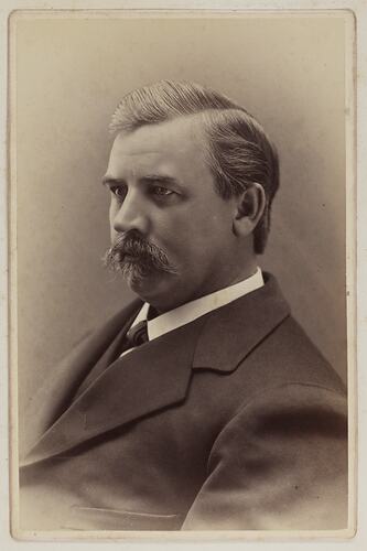 Three quarter bust portrait of man wearing dark suit and white shirt.