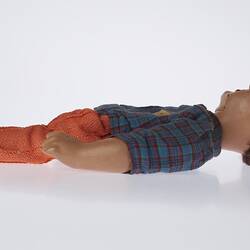 Left profile of laying doll. Red pants, blue top, short brown hair.
