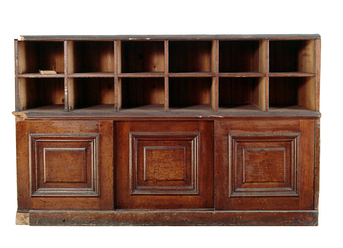 Panelled wooden pharmacy counter with medicine shelves.
