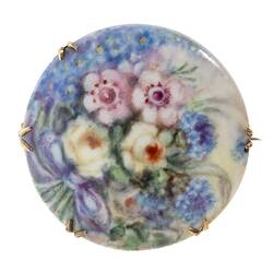 Round painted porcelain brooch with floral posy of wildflowers in pink, yellow, blue.