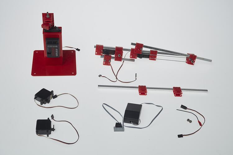 Red and black plastic components with cables that make up a toy robotic arm.