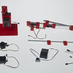 Red and black plastic components with cables that make up a toy robotic arm.