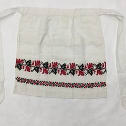 White hessian cotton with long ties, red and black leaf and vine embroidered pattern across front lower section.