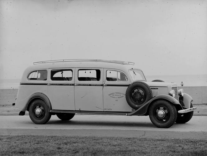Motor bus with grass in foreground, water (ocean?) in background.