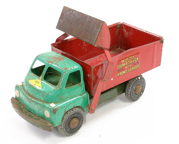 Metal toy dump truck with green cabin and red tray. Red moveable shovel on arms above cabin. Yellow lettering