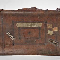 Worn brown leather suitcase with multiple labels, two reading fragile.