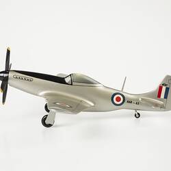 Model plane painted silver. Blue, white, red roundel on sides. Red, white, blue flag on tail. Front black four blade propeller. Three wheels. Profile.