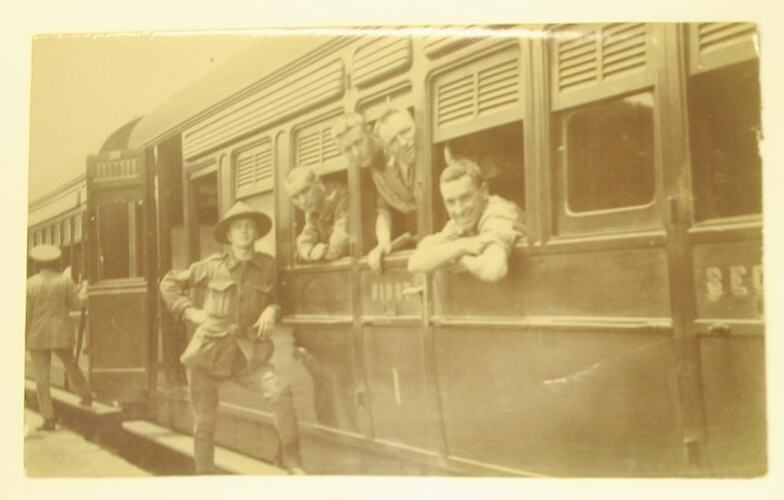 Men in military uniform leaning out of, standing next to stationary train.