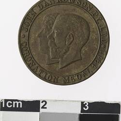 Round bronze coloured medal with profile of a man and woman, text surrounding.