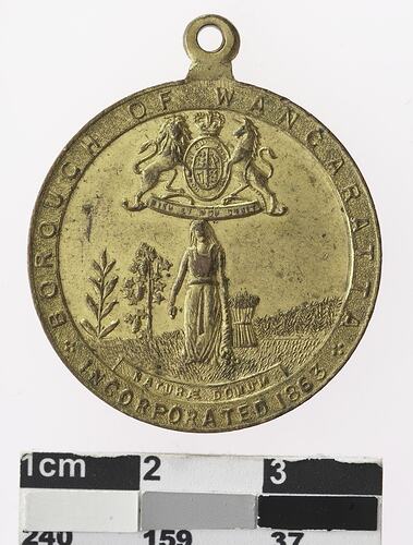 Gold coloured medal with image of woman and coat of arms.