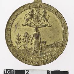 Gold coloured medal with image of woman and coat of arms.