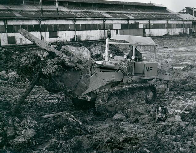 A man driving a crawler loader, clearing an industrial work site.