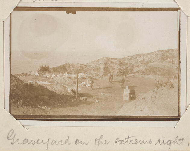 Hilly landscape with graveyard on the left and servicemen in cleared area on the right.