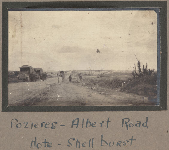 Two trucks and a group of servicemen on the side of a dirt road.
