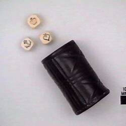 Cylindrical leather cannister and three ivory dice with symbols of crown, anchor, heart on face.