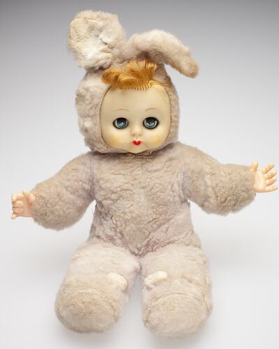Doll with vinyl face and hands with pale pink cloth bunny suit body and synthetic hair. Eyes open.