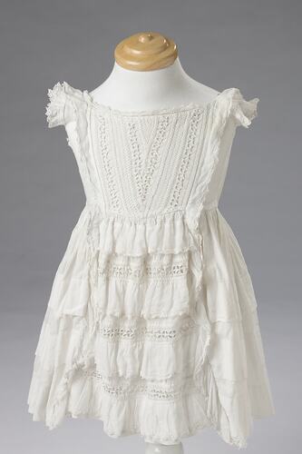 White cotton girls sleeveless dress with ruffles at shoulders.