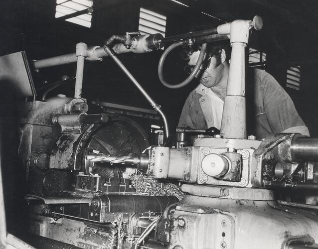 A man wearing safety glasses is operating a large lathe.
