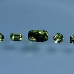 Five green faceted gemstones, various shapes.