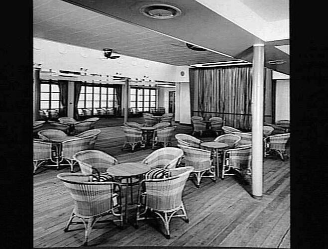 Ship interior. Room with round cane chairs and square tables. Windows in background.