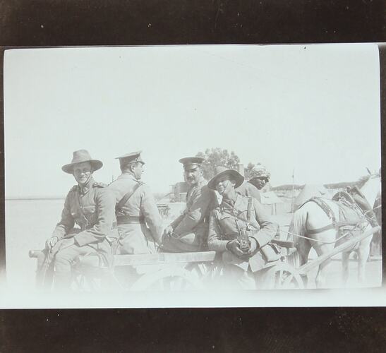 Men in uniform sitting on the back of a horsedrawn cart.