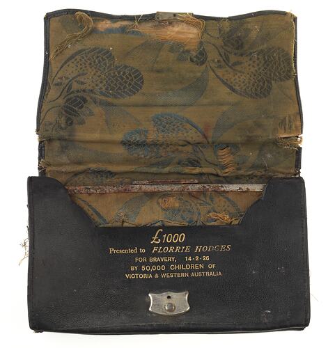 Open leather purse with discoloured interior woven cloth and gold lettering printed on leather above clasp.