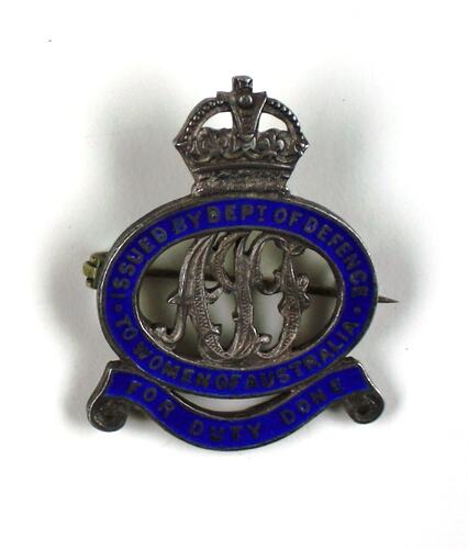 Grey metal badge with blue enamel detail surrounding cut-away metal letters, crown on top.