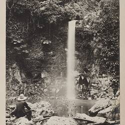 Man at rock pool below waterfall.