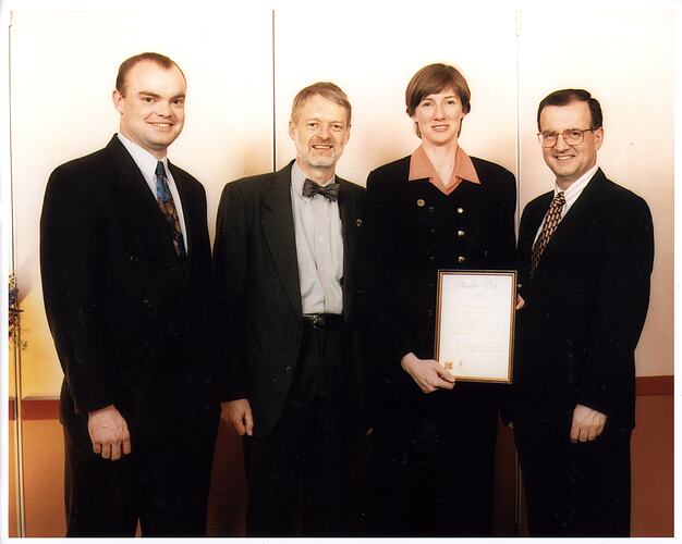 Group in suits with woman holding framed certificate.