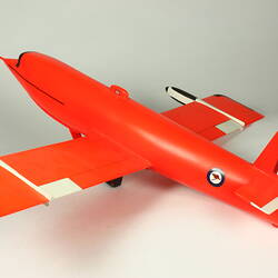 Orange pilotless aeroplane model with antenna attached to nose and a single skid in place of wheels.