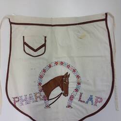 White apron with brown trim. Brown embroidered horse head framed by inverted floral horseshoe.