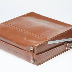 Back of tan leather carry case with leather handle and silver trim.