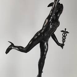 Metal statue of figure standing on an orb carrying a lamp and caduceus. Right view.