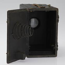 Black box shaped camera with open end. Spring attached to inside of open door.