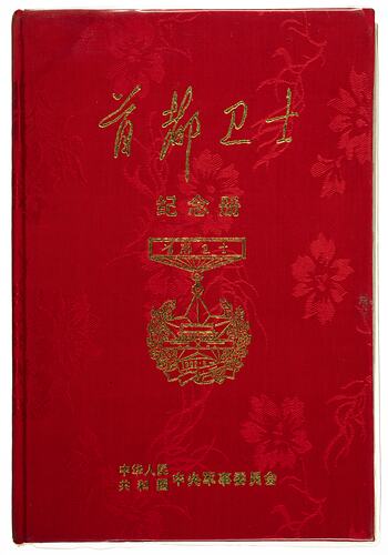 Front of hard cover red book with gold characters and outline of medal.