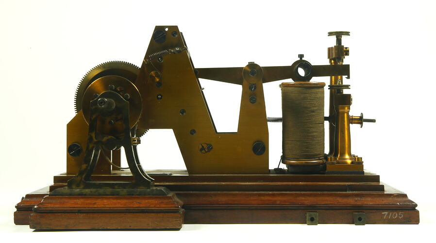 Brass apparatus with batteries on wooden base, side view.