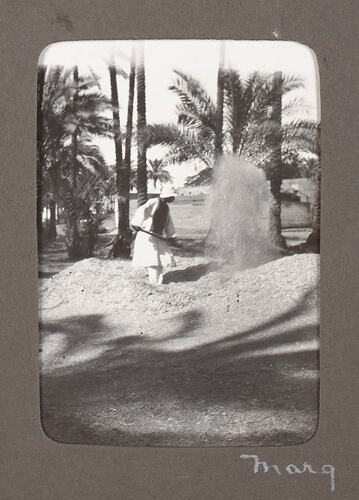 Man winnowing grain near palm trees.