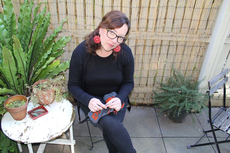 Woman seated in courtyard, crocheting.